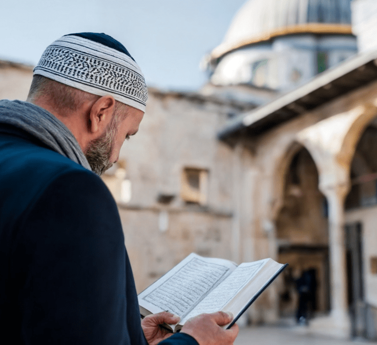 Hombre musulmán leyendo el Qurán con una mezquita al fondo durante el amanecer o anochecer