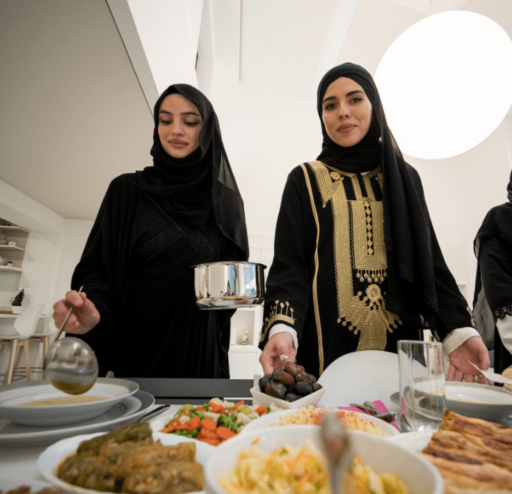 Sawm – Ayuno y Espiritualidad Dos mujeres musulmanas preparando y sirviendo comida para el rompimiento del ayuno en Ramadán