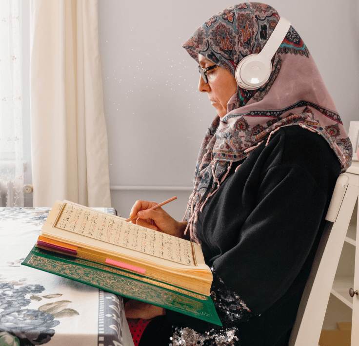 Mujer musulmana leyendo el Qurán con auriculares escuchando su recitación